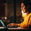 Person in yellow sweater uses a laptop computer in a dark room.