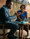 Two people sit and talk. There is a tablet and coffee cup on the table.