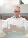 A person with glasses relaxes and looks at a tablet in an office.
