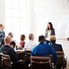 Multiple students sit in seats as two people stand in front of a whiteboard.