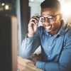 An employee at their desk in an office setting, smiling at their desktop monitor as if talking on a video call.