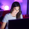 A woman smiling while looking at a computer screen in a room with purple lighting.