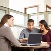 Three people sit around a laptop in an office cubicle.