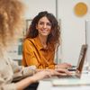 Two women sit in a creative colorful office, working on computers.