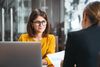 Two people in an office setting sit at a desk, reviewing metrics in a bar graph.