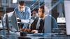Three people sit in an office collaborating together on computer screen.