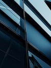 A dark blue building featuring a prominent glass wall reflects light, which emphasizes its architectural design.