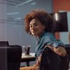 Person sits in conference room, turned around in seat and smiles at camera.