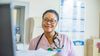 Medical professional wearing pink scrubs and a stethoscope smiles in a healthcare setting.
