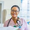 Medical professional wearing pink scrubs and a stethoscope smiles in a healthcare setting.