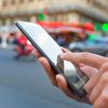 Person holds a mobile phone while walking on a city street.