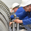 Two industrial workers in hard hats work on turbines.