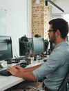 Person in business casual attire in an office environment typing on a computer keyboard.