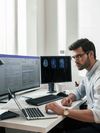 Healthcare worker checks laptop while processing electronic documents.