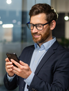 Person with glasses smiles and looks at a mobile phone.