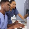 Two medical professionals in scrubs collaborate on medical images on a computer screens.