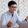 Person in conference call on laptop in front of a white brick wall.