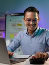 Asian businessman in glasses smiles as he works on his laptop in an office.