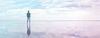 Person stands on reflective ground, looking at blue and pink sky and clouds.