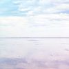 Person stands on reflective ground, looking at blue and pink sky and clouds.