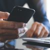 Close photo of a person holding a cell phone while working on a laptop.