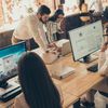 Group of young professionals work and collaborate on desktop computers in an open office.