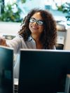 Business professional in glasses smiles while working in front of two computer monitors.