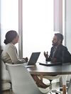 Two people discuss business in an office conference room.