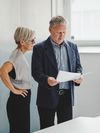 Two people stand in an office and look at paperwork.