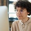 Person with curly hair and a collared shirt sits in front of a computer monitor.