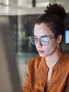 Person in glasses stares at a computer screen. 