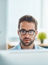 Person in glasses sitting at a desktop computer.