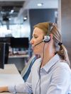 A person with a headset sits and talks in an office.