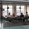 Four people sit in a glass conference room.