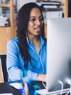 Person with glasses and headphones sits and looks at a computer monitor.