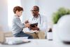 Energetic cheerful male doctor grinning while showing tablet to boy and sitting