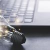 Light bulb with sparks around it sits near a laptop.