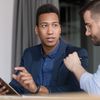 Two people sit in discussion, with one holding a tablet computer.
