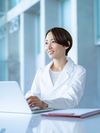 A woman smiles with her laptop in front of her in a bright, modern office.