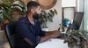 Person sits at desktop computer with houseplants on desk.