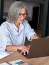 A person wearing glasses sits and types on a laptop. There is a notebook on the table.