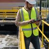 Person in a white hard hat and a hi-viz vest on site using a tablet.