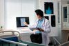 Doctor pointing at computer screen while holding medical records in hospital room