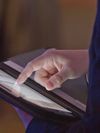 Close-up photo of a hand touching a tablet computer screen.