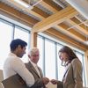 Three people stand in a wood and glass office.
