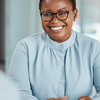 Person with glasses and a pen in hand smiles in an office setting.