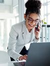 A woman in a business suit smiles confidently while holding a tablet, standing next to an office window.