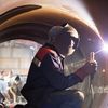 Welder in protective vest and helmet welds metal.