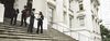 Four people stand on the stairs of a government building.