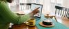 Person uses laptop at breakfast table with pot of coffee and coffee mug nearby.